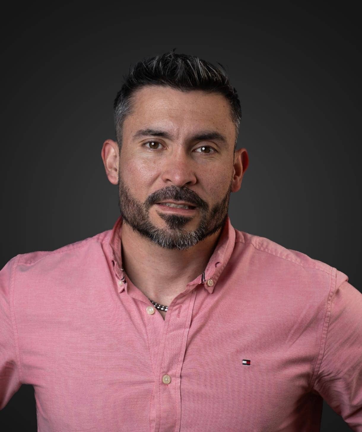 Retrato de Justo Miguel Vargas, de camisa rosa, sobre un fondo oscuro.